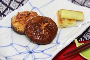 テーブルクロスの上に置かれた長皿に盛られているしいたけのつくね焼きと箸置きに置かれた箸の写真