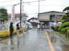 雨の中、傘をさした保護者たちが生徒たちの登校を見守っている写真