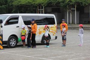 校庭に置かれた車の横に並んで立っている子どもたちの写真