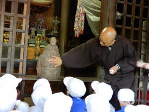 住職から木の仏像の説明を聞いている子どもたちの写真