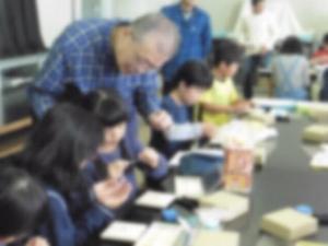 男性と一緒に机の上で小物を製作する生徒たちの写真