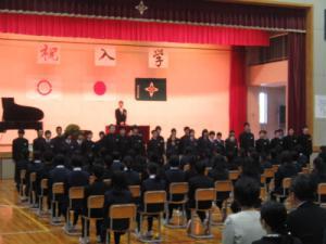 入学式の体育館で多数の生徒の前で男性が式辞を述べている写真