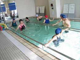 プールで手すりを使いながら水中運動する高齢者たちの写真