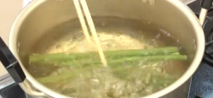 お湯の沸いている火にかけた鍋でふきをゆで菜箸で混ぜている写真