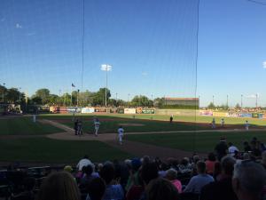 青く晴れた空の下で、野球の試合を行う選手らと観客席を観客席から撮影した写真