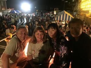 太鼓祭りにて、夜に並んだ屋台をバックに撮られた、外国人夫婦と日本人夫婦の写真