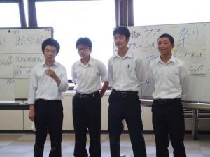 手に持った紙の資料とホワイトボードを元に発表を行う男子中学生4人の写真