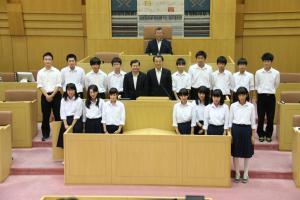 岡谷市役所議場にて、スーツを着た男性3人とその両脇に並ぶ16人の中学生の集合写真