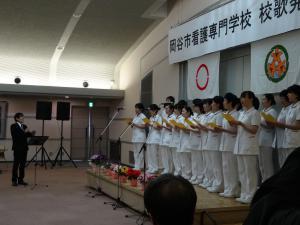 指揮をする平尾昌晃さんと校歌を斉唱する生徒たちの写真