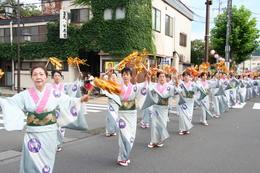 金色の飾りを両手に持って着物姿で市内を練り歩く流し踊りの写真