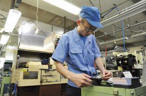 工場内で作業着を着て機械を操作する男性の写真