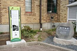 旧岡谷市役所庁舎のスタンドサインと石碑が直角に並んで立っている写真