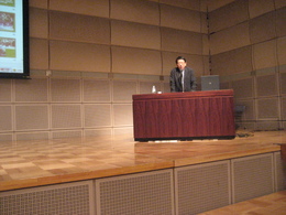 ステージの上の演壇で講演をする男性の写真