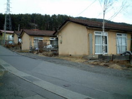 道路の横に並ぶ茶色の屋根に薄茶色の壁の家の団地の写真