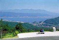 遠くに見える山並みと諏訪湖を望む高台にベンチが置かれた塩嶺王城パークラインの展望所の景色の写真