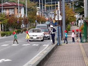 赤い帽子をかぶった生徒たちが横断歩道の渡り方の指導を受けている写真