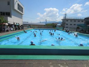 青空のもとプールで子どもたちが泳いでいる写真