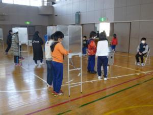 体育館の中で子どもたちが児童会役員を決める選挙の投票をしている写真