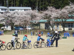 校庭で自転車に乗る生徒たちと指導する警察官の写真