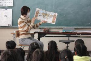 教室で座っている子どもたちの前で絵本を持って話をする女性の写真