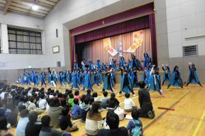 体育館のステージ前で子どもたちが青い衣装を着て踊っている写真