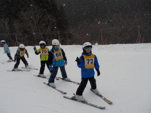 ゼッケンをつけた子どもたちがスキー場でストックなしで滑っている写真