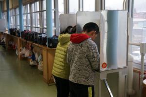 廊下に設置された投票場で記入している子どもの写真