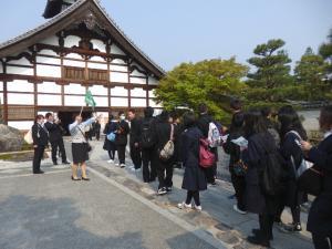 修学旅行でガイドが案内して多数の生徒が並んで歴史的建造物の建物に入っていく写真