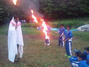宿泊学習で複数の生徒と白い布を被った男性が炎のついた棒を持っている写真