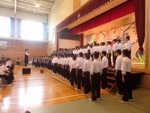 体育館で生徒たちが指揮に従って合唱をしている写真