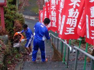 神社の石の階段で1人の生徒がほうきを持ちもう1人の生徒がゴミを捨てている写真
