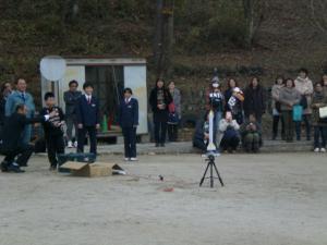 グラウンドで大人と子どもがロケットを発射させようとしている写真