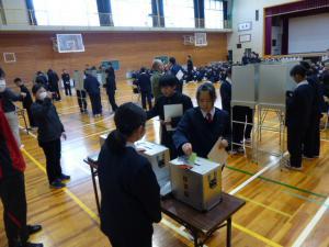 体育館に設置された投票箱に多数の生徒が票を入れている写真