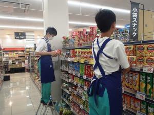 スーパーの商品棚で二人の男子生徒が作業をしている写真