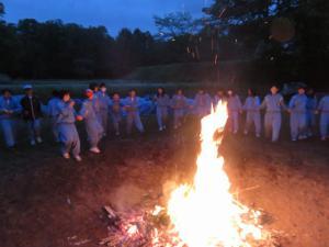 生徒たちがキャンプファイヤーの火を取り囲んでいる写真