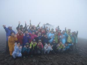霧のかかった硫黄岳の山頂で生徒たちが集合してポーズをとっている写真