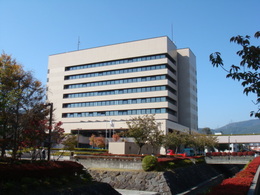 青空の下、木々に囲まれた岡谷市役所外観の写真